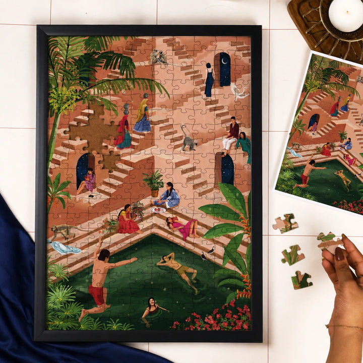 A framed jigsaw puzzle featuring a detailed, colorful illustration of people relaxing by a pool in a tropical setting, displayed on a white tiled surface with loose puzzle pieces and a hand visible at the right edge.